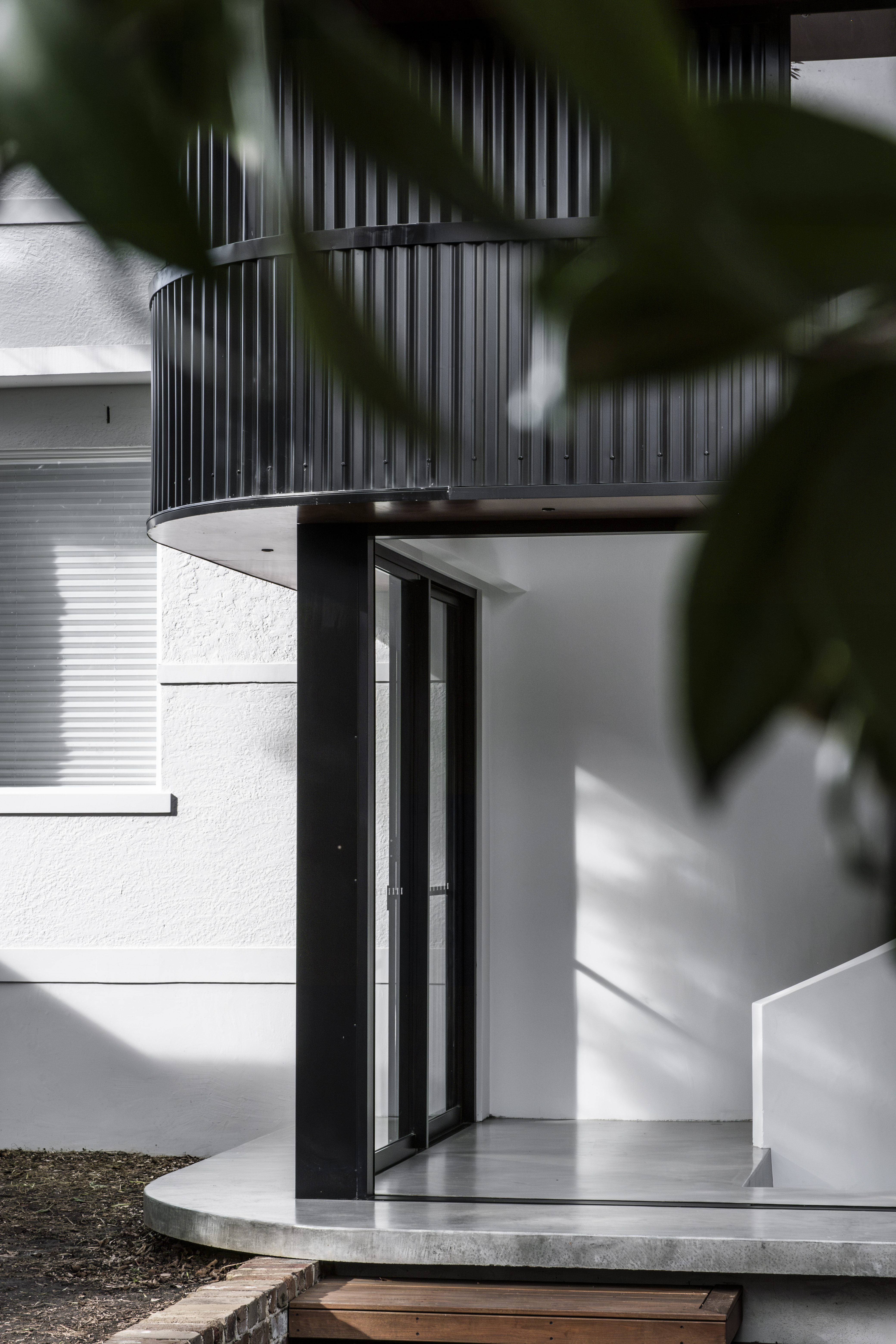 Exterior entry — curved black metal cladding with glass door and concrete platform