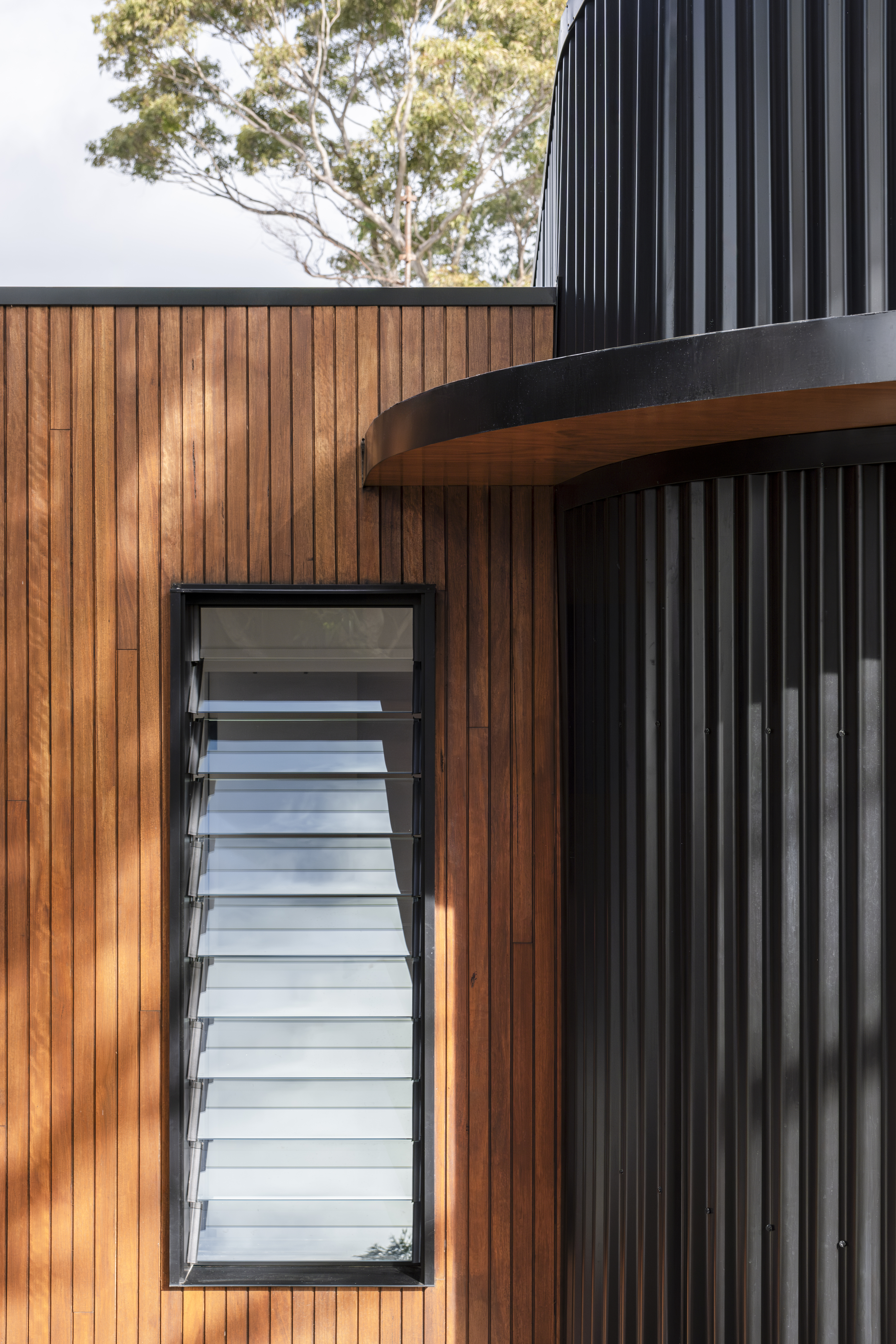 Exterior detail — timber cladding with louvre window next to black curved cladding
