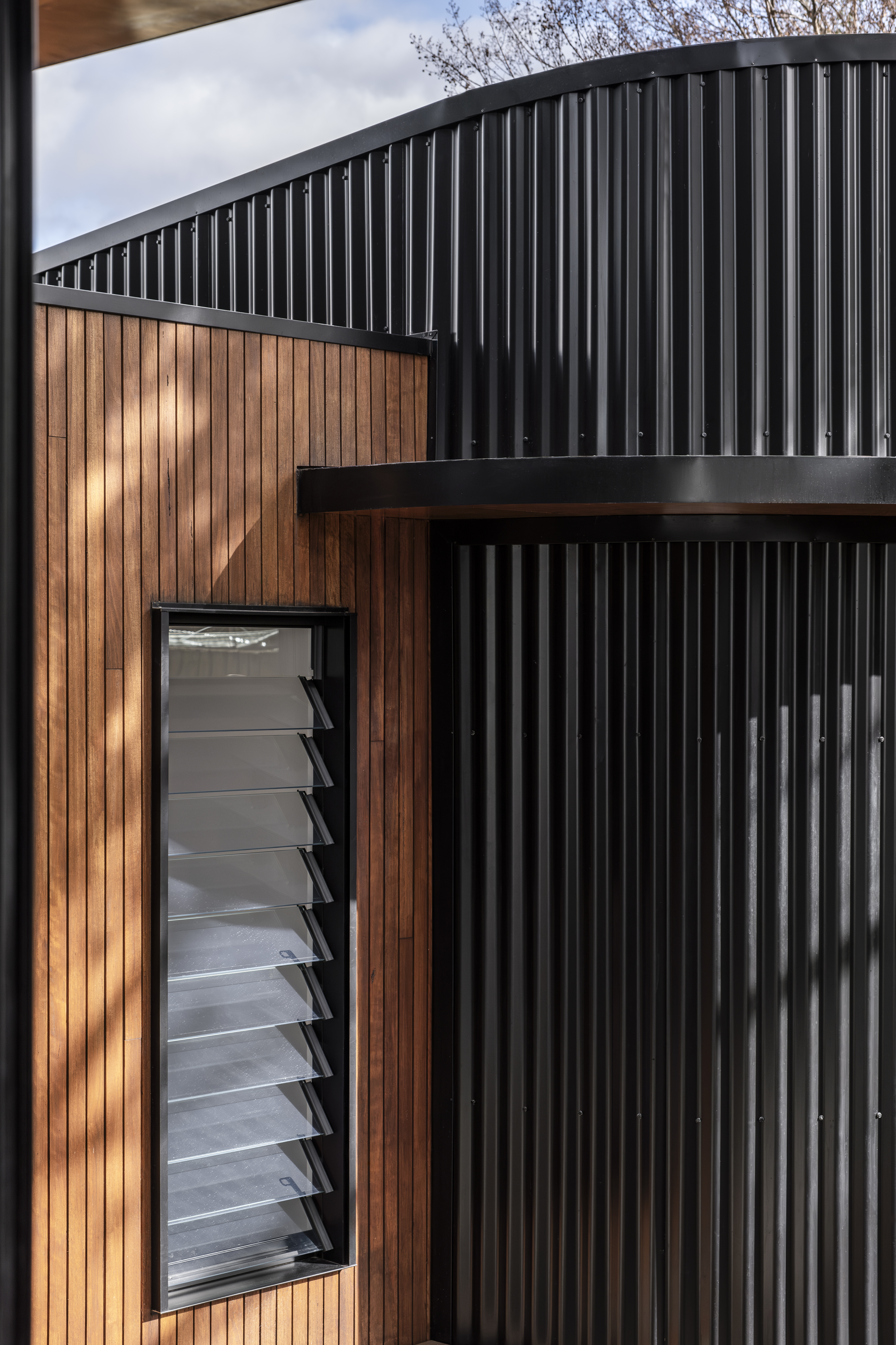 Exterior detail — timber and black corrugated cladding with louvre window