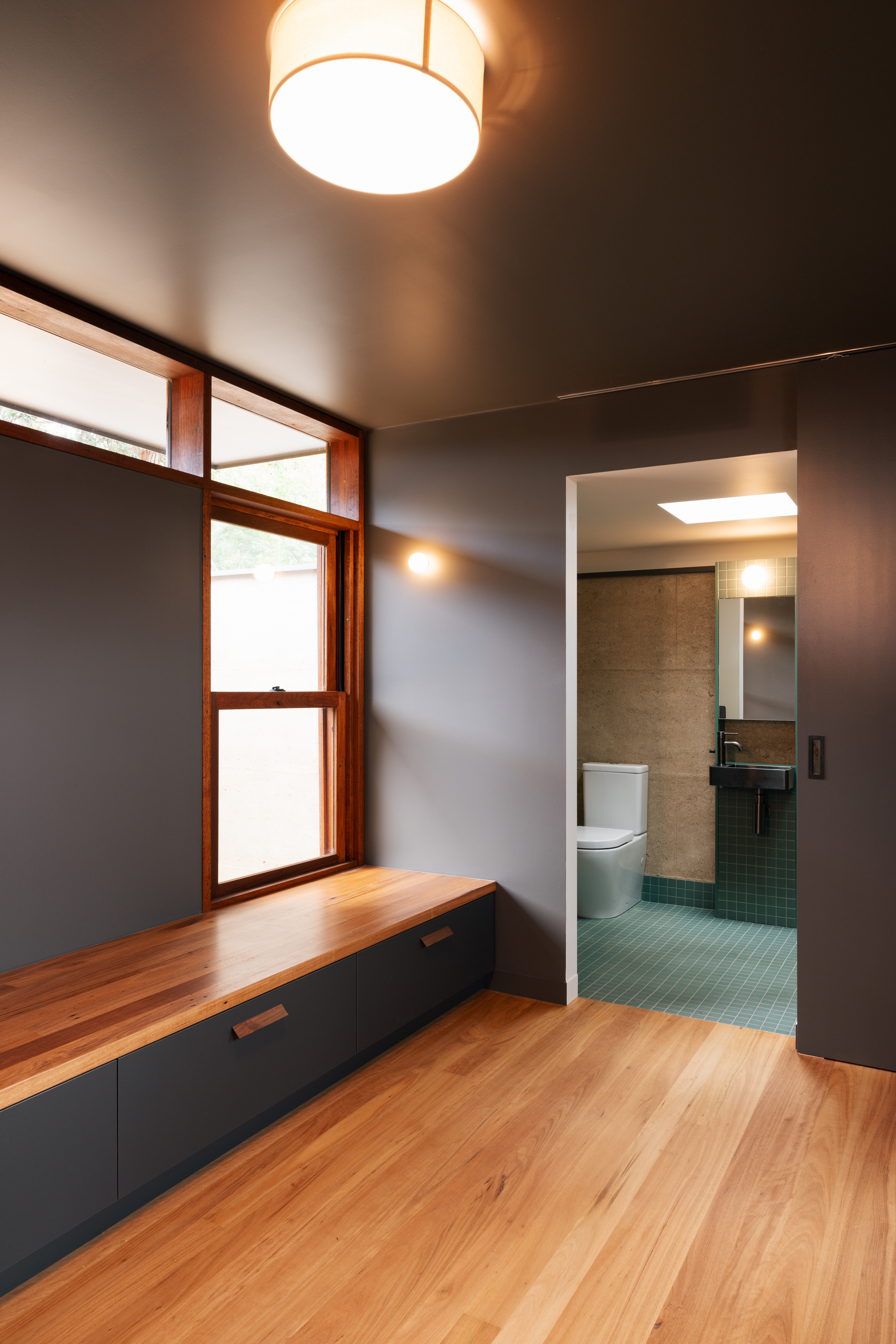 Bedroom — built-in timber bench seat, hardwood floors and bathroom beyond