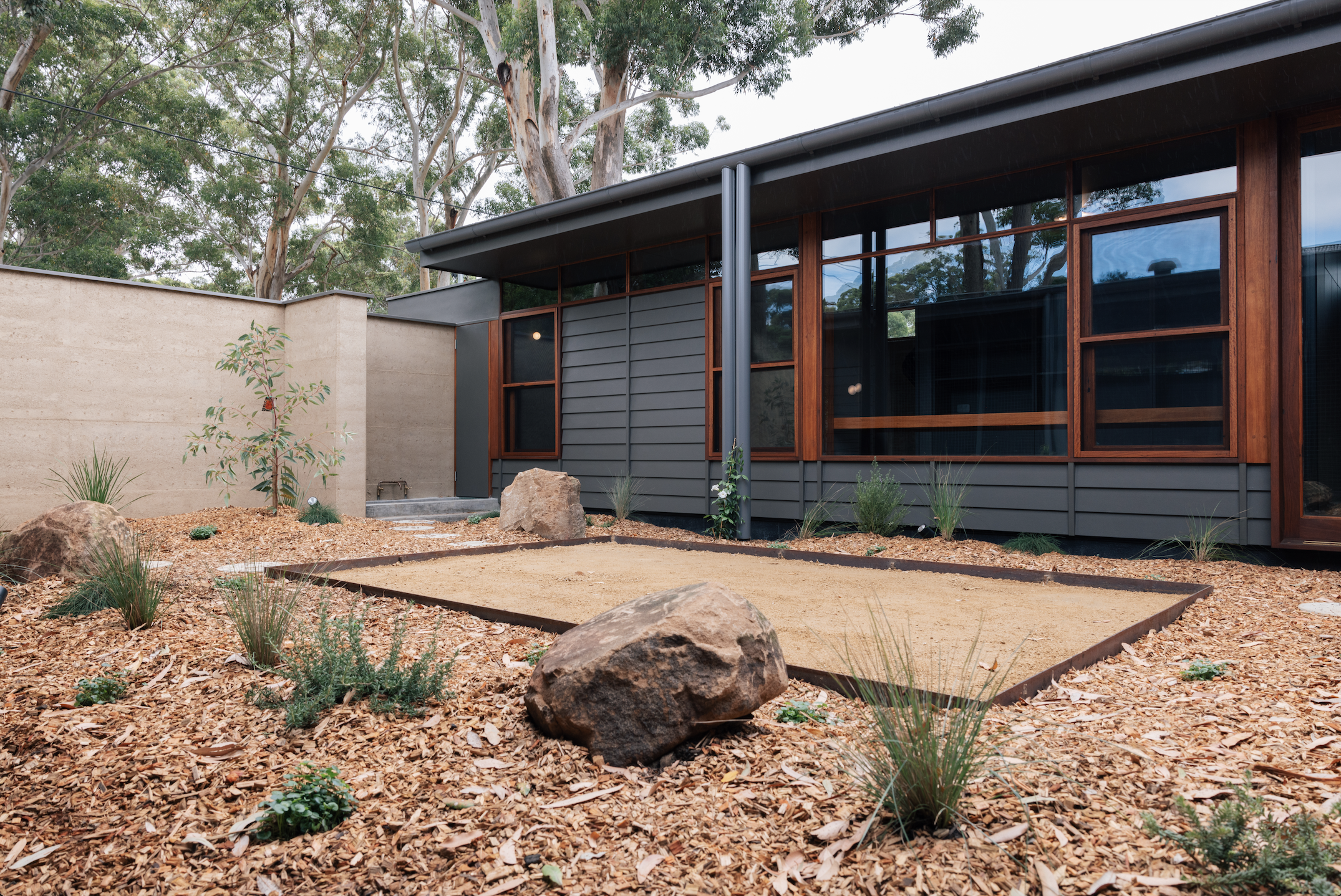 Courtyard — native garden with rammed earth wall, dark cladding and hardwood-framed windows