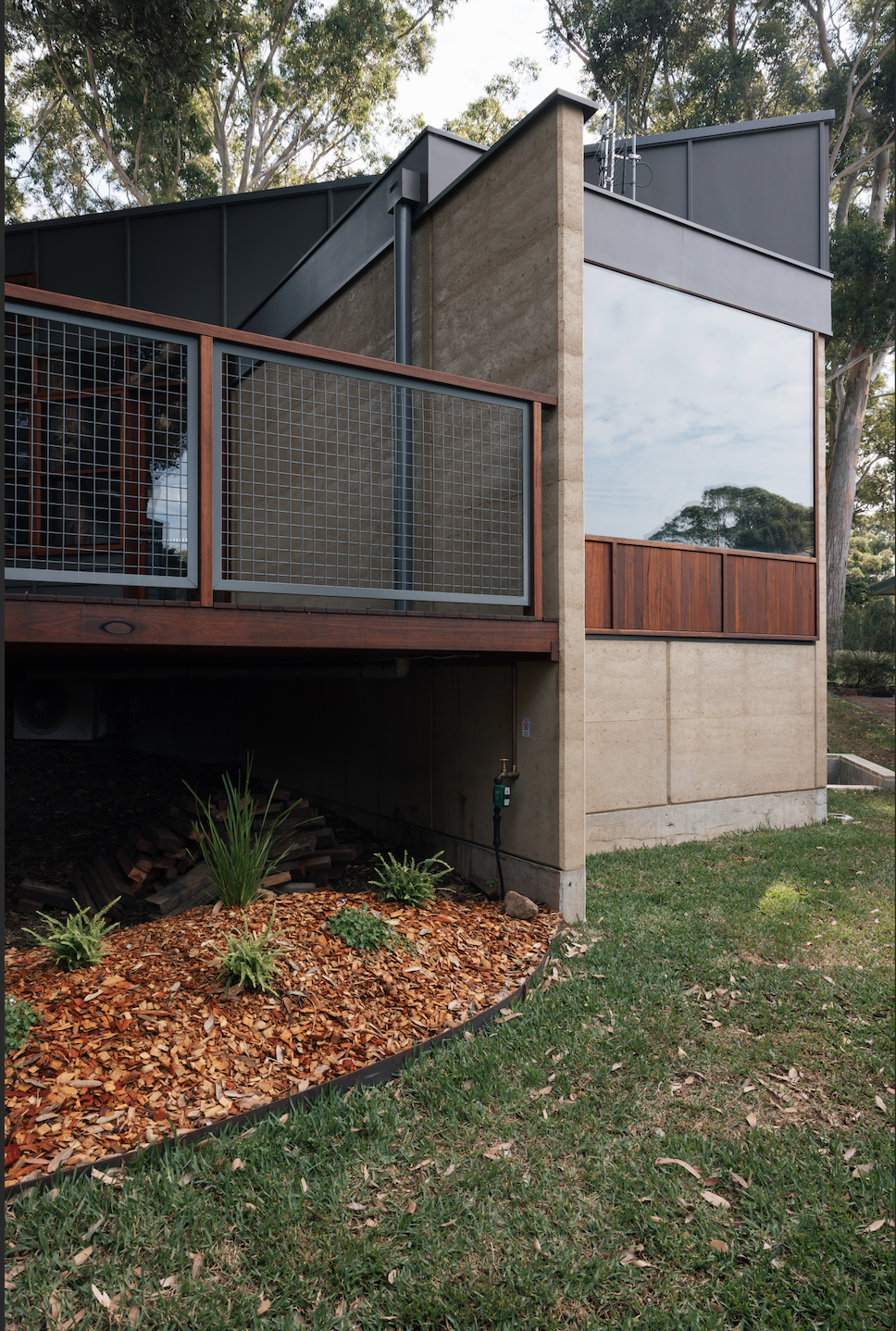 Exterior corner — rammed earth pier, hardwood deck with mesh balustrade and timber cladding