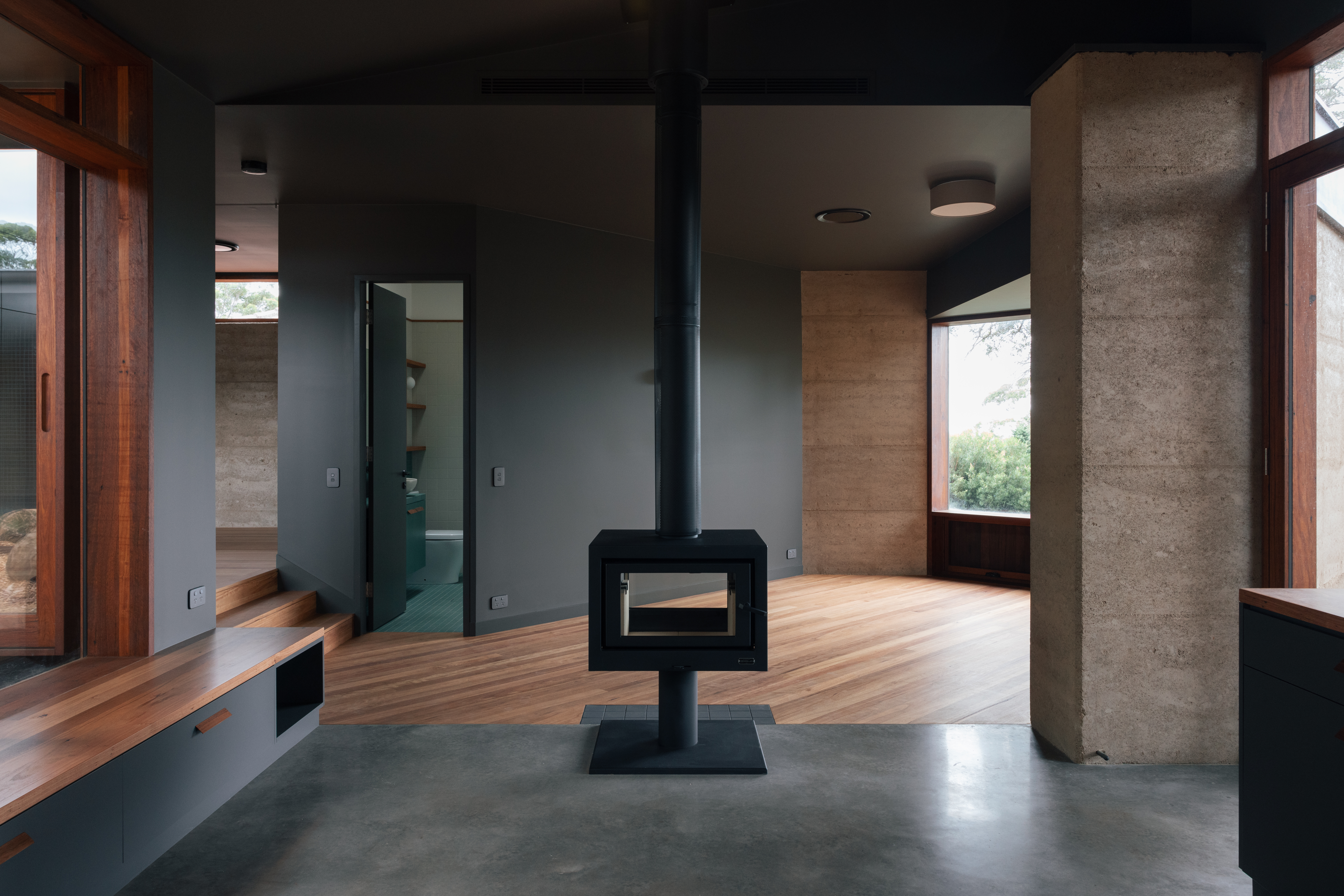 Boorea House interior — freestanding fireplace, rammed earth wall, polished concrete and timber floors