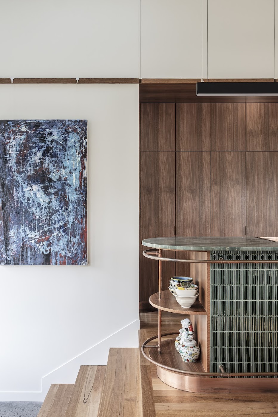 Kitchen detail — abstract painting on white wall, walnut joinery and green tile island end with copper shelving